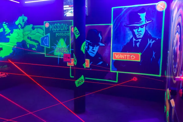 Wand mit Weltkarte, Gangster-Porträts und Wanted-Plakat, davor rote Laserstrahlen