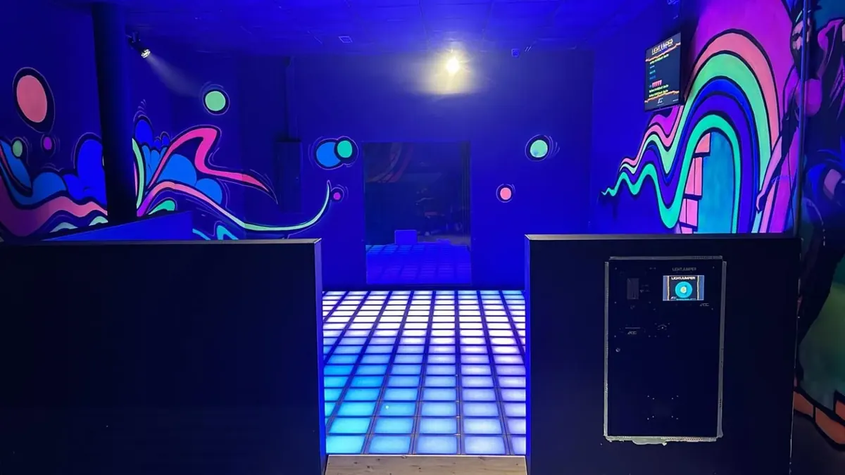Light Jumper: Bodenfeld aus blau leuchtenden LED-Platten vor bunten Schwarzlicht-Wandbildern